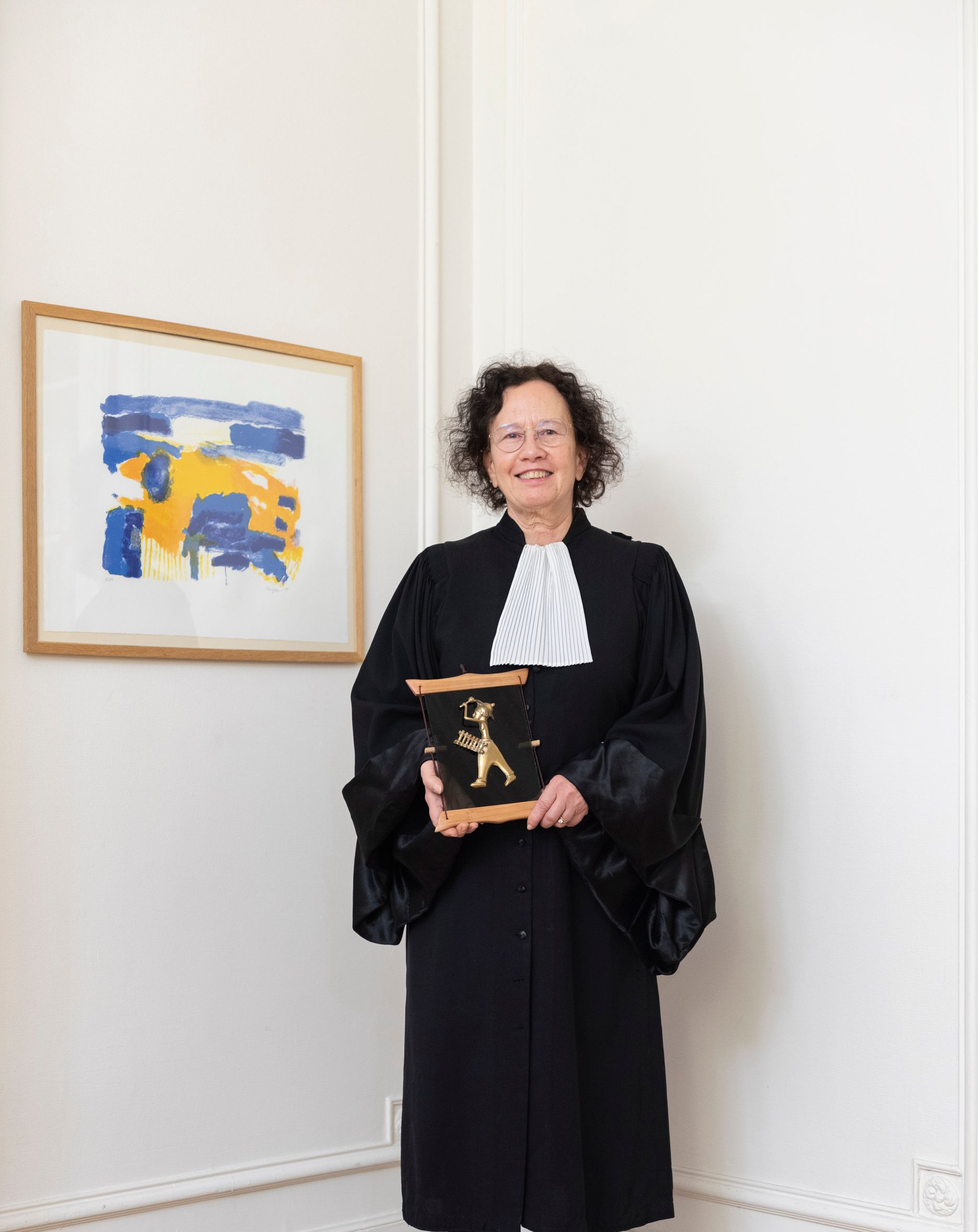 Une personne en robe noire tient un prix encadré à côté d'un tableau coloré dans une galerie.