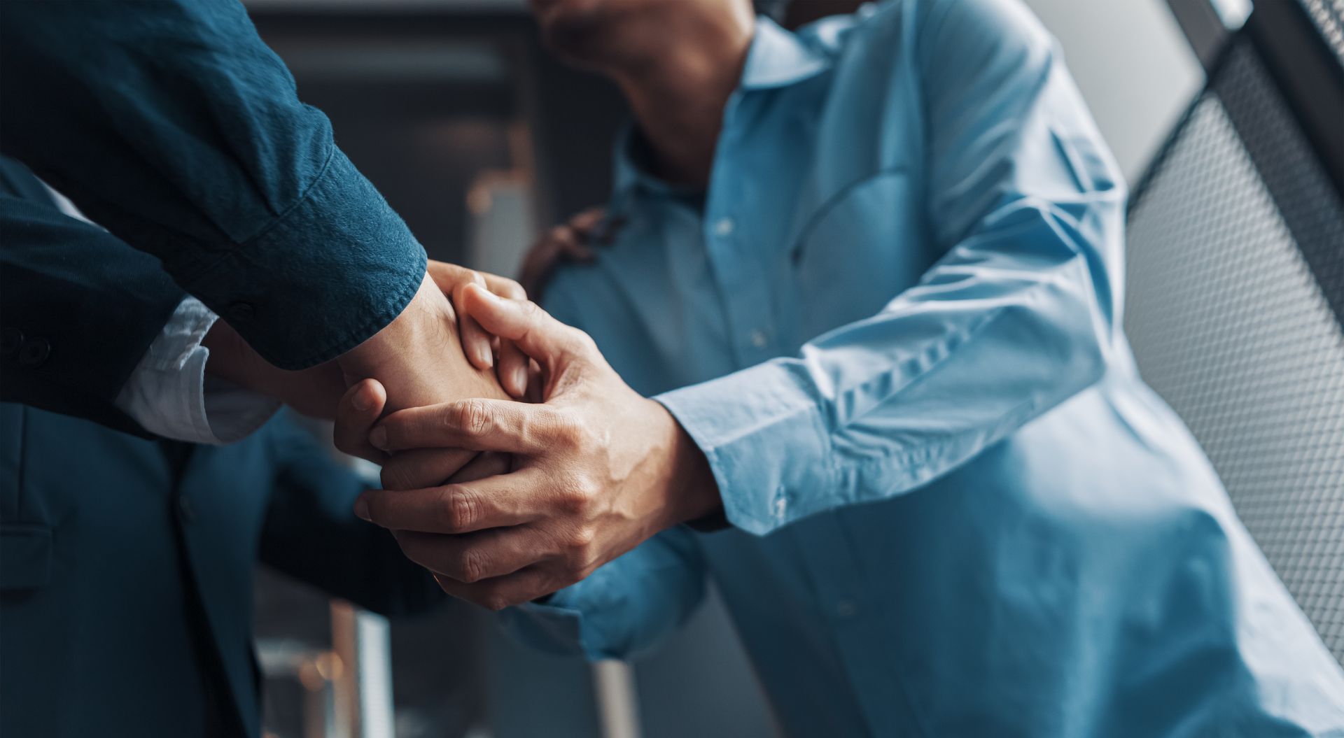 Deux personnes se serrent la main dans une poignée de main amicale, l'une d'elles est assise et porte une chemise bleue.