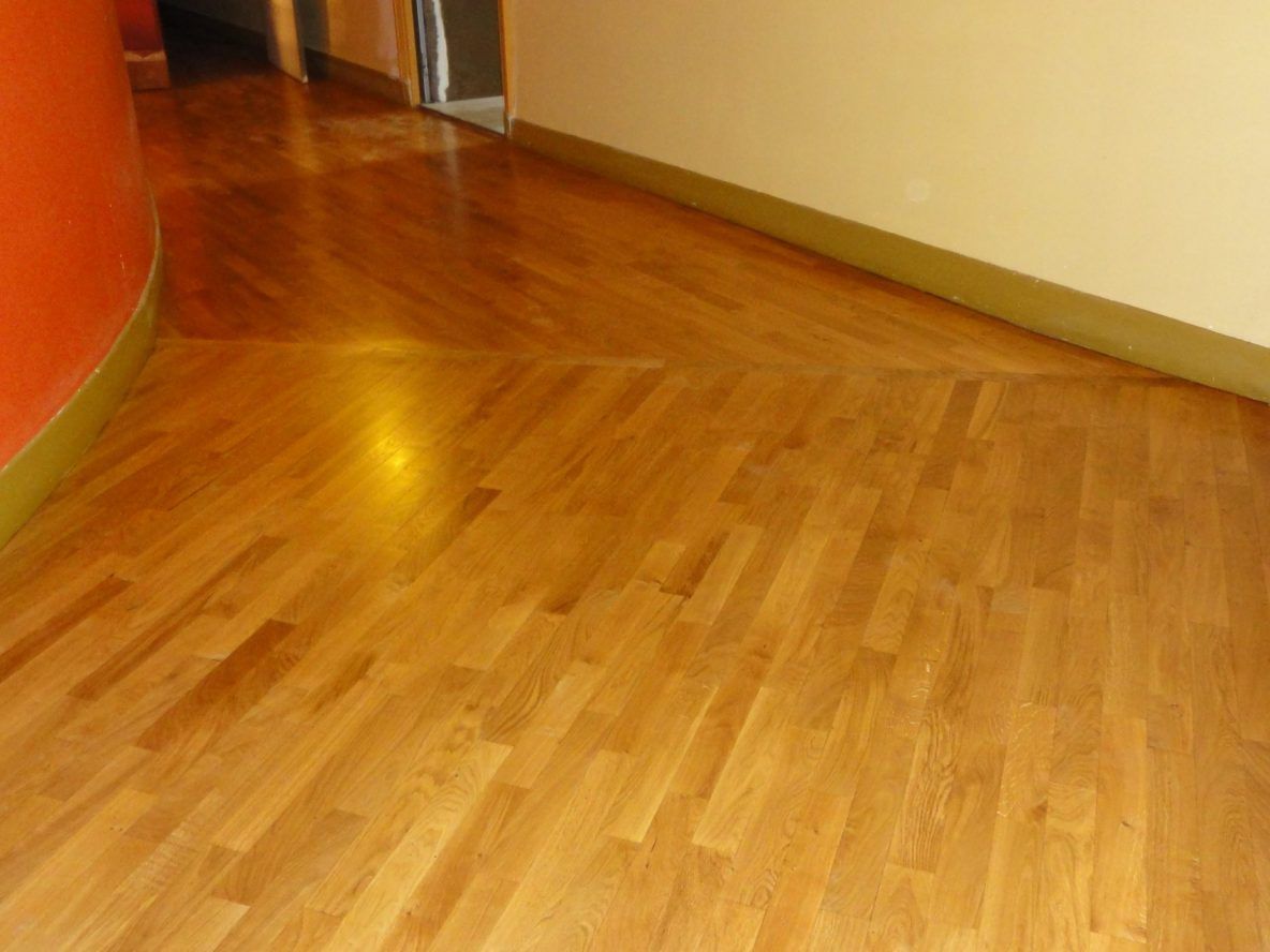 Vue grand angle d'un couloir avec parquet en bois clair, un mur orange incurvé et des murs beiges unis.