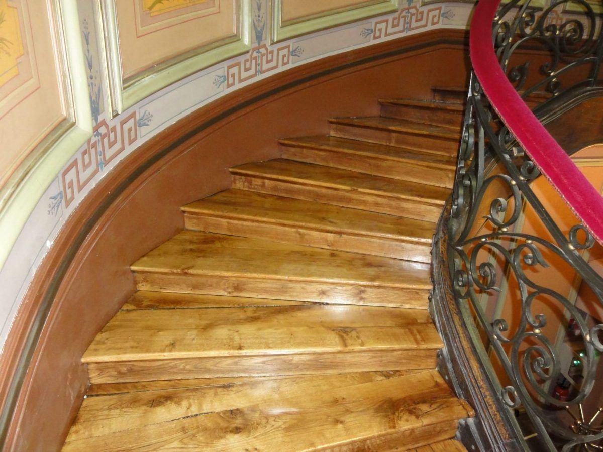 Un escalier en bois incurvé avec une rampe en fer forgé ornée et des détails de moulures peintes sur le mur.