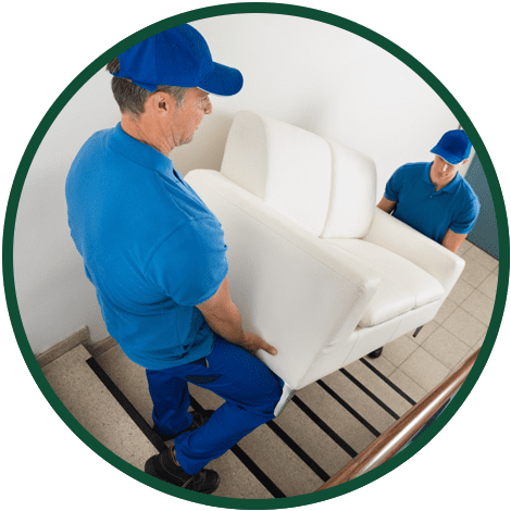 Deux déménageurs en uniforme bleu montent un fauteuil blanc dans un escalier.