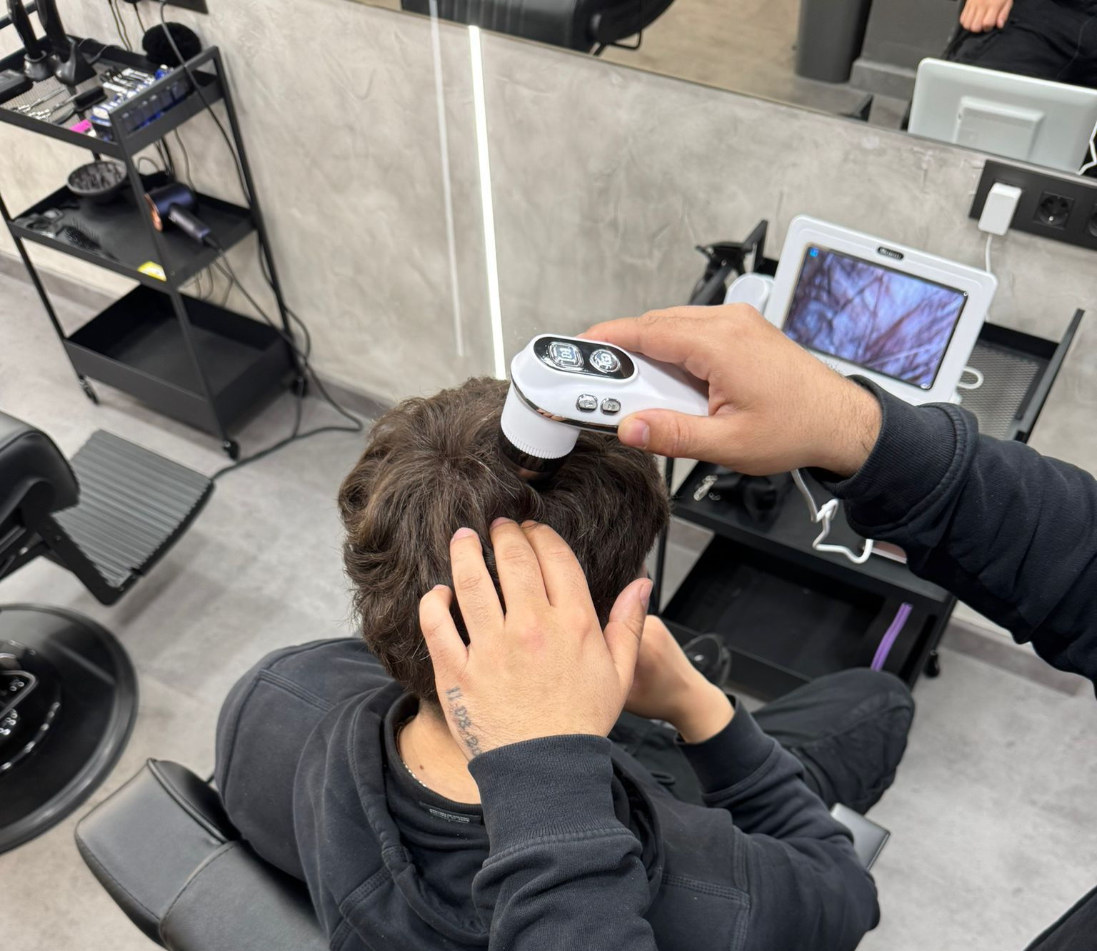 Una persona en una silla de barbero tiene una toalla caliente en su cara, sostenida por otra persona.