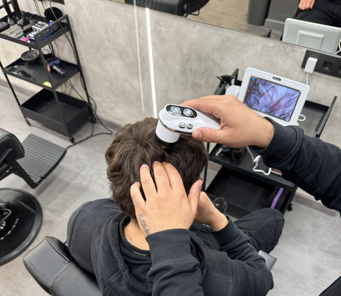 Una persona en una silla de barbero tiene una toalla caliente en su cara, sostenida por otra persona.