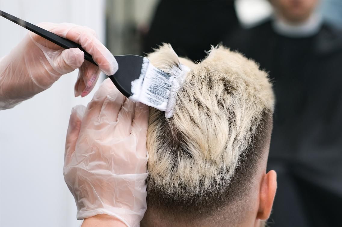 Peluquera aplicando decolorante al cabello rubio de una clienta, usando guantes.