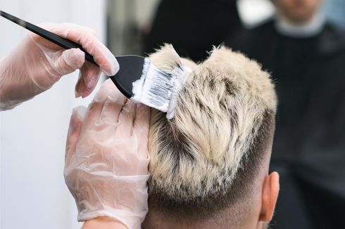 Peluquera aplicando decolorante al cabello rubio de una clienta, usando guantes.