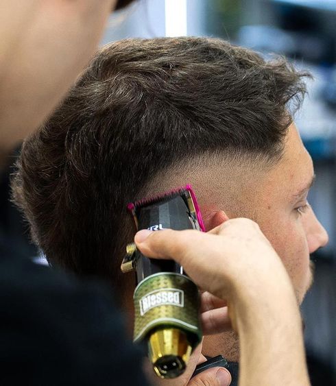 Un barbero recorta el cabello oscuro de un hombre en un lateral con una maquinilla eléctrica.
