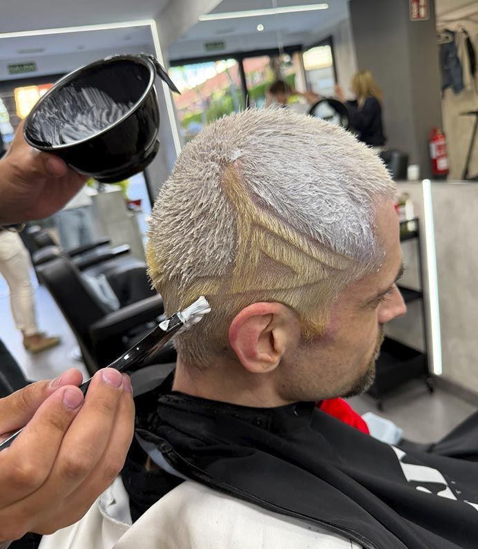 Peluquero rociando decolorante sobre el cabello corto rubio platino de una clienta en un salón de belleza.