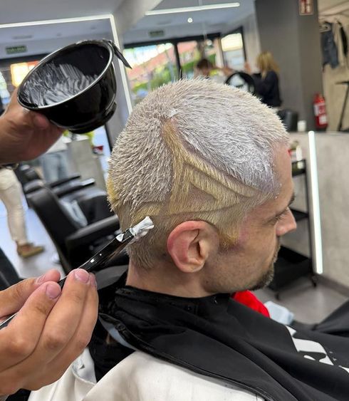 Peluquero rociando decolorante sobre el cabello corto rubio platino de una clienta en un salón de belleza.