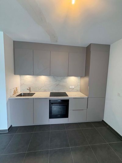 Personne se tenant dans une cuisine en rénovation en désordre, entourée de matériel de peinture et de placards inachevés.