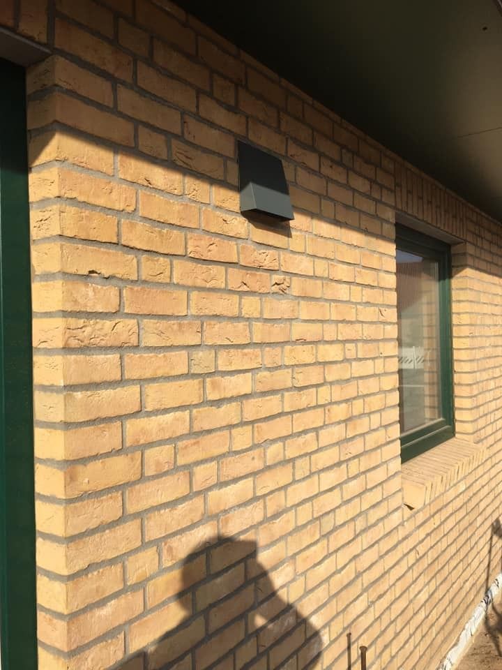 Außenwand aus Ziegelsteinen mit kleinem schwarzen Lüftungsschlitz und einem Fenster im Sonnenlicht
