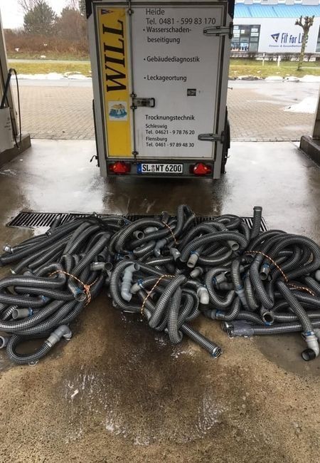 Vor einem Anhänger auf nassem Asphalt lagen gestapelte schwarze Schläuche, hinten prangte ein gelbes „WILL“-Schild.