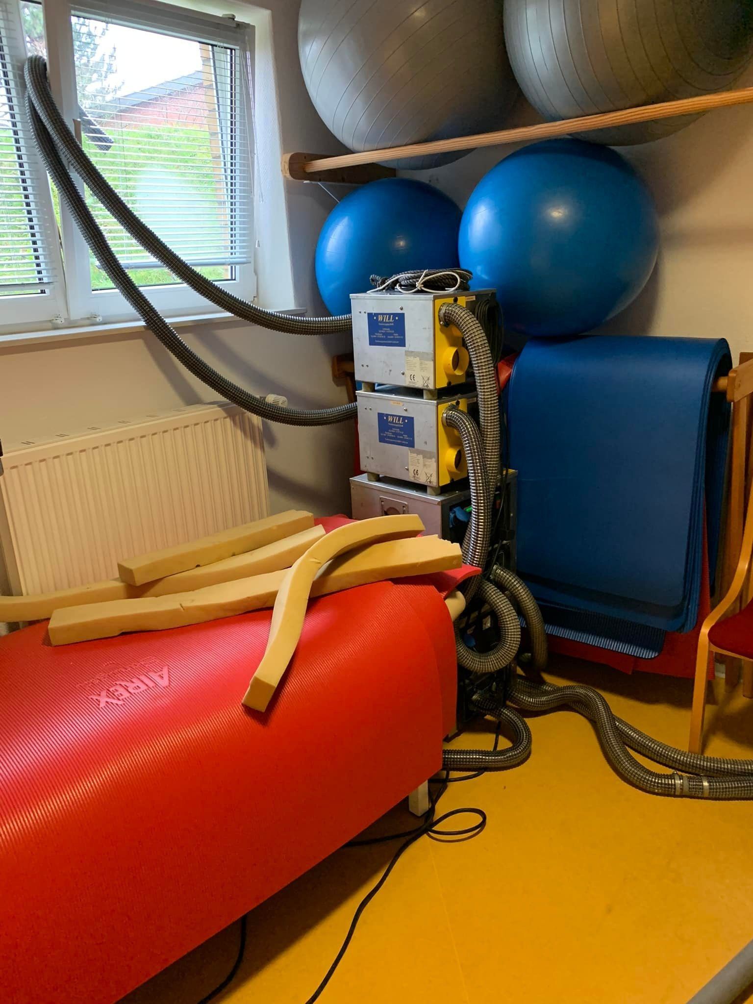 Physiotherapieraum mit roter Therapiematte, blauen Gymnastikbällen und Fitnessgeräten am Fenster