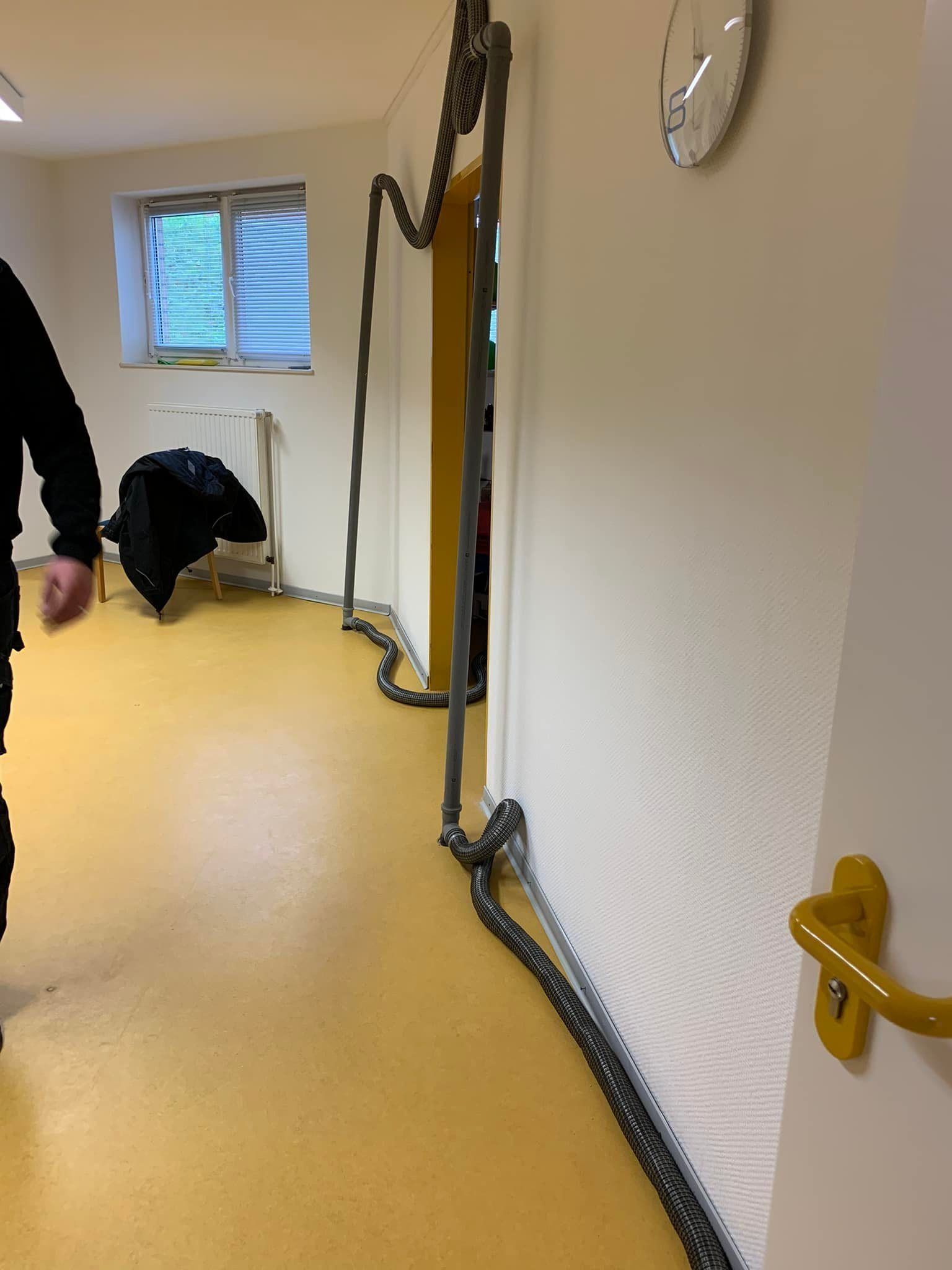 Ein schmaler Flur mit gelbem Boden, aufgerollten Kabeln an der Wand und einer Person, die in der Nähe des Fensters kauert.