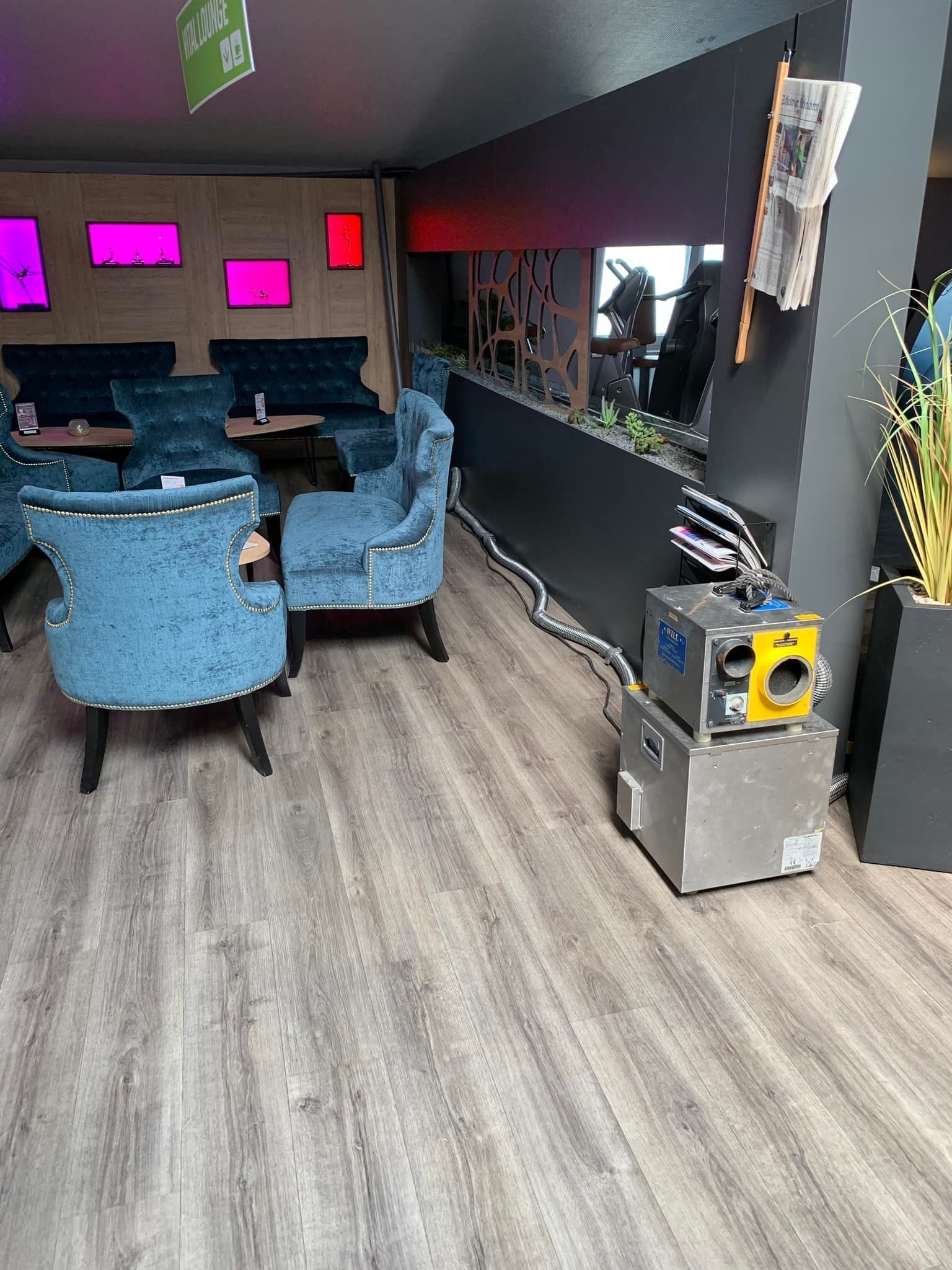 Moderne Lounge mit blauen Sesseln, rosa Paravents, Holzboden und einer Kaffeemaschine auf der Theke