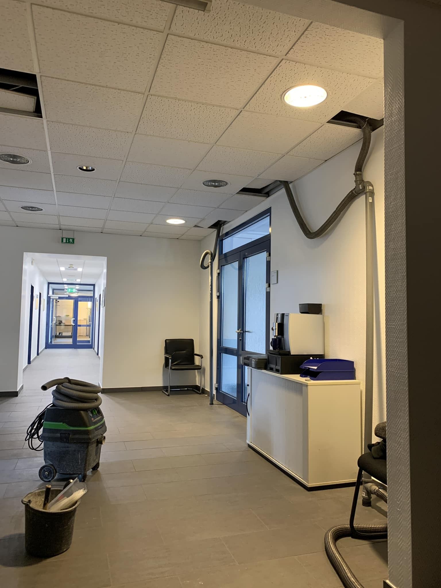 Leerer Büroflur mit Deckenarbeiten, einer Leiter und Reinigungsmitteln an der Wand