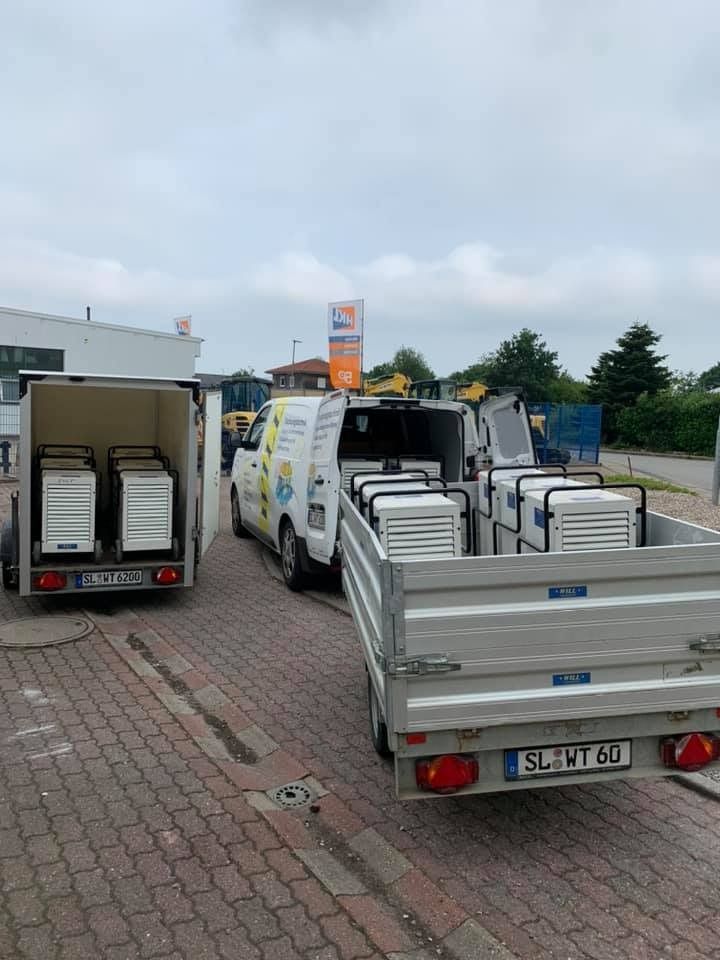 Weiße Lieferwagen mit offenen Hecktüren und gestapelten Metallpaletten parkten im Freien auf einem gepflasterten Parkplatz.