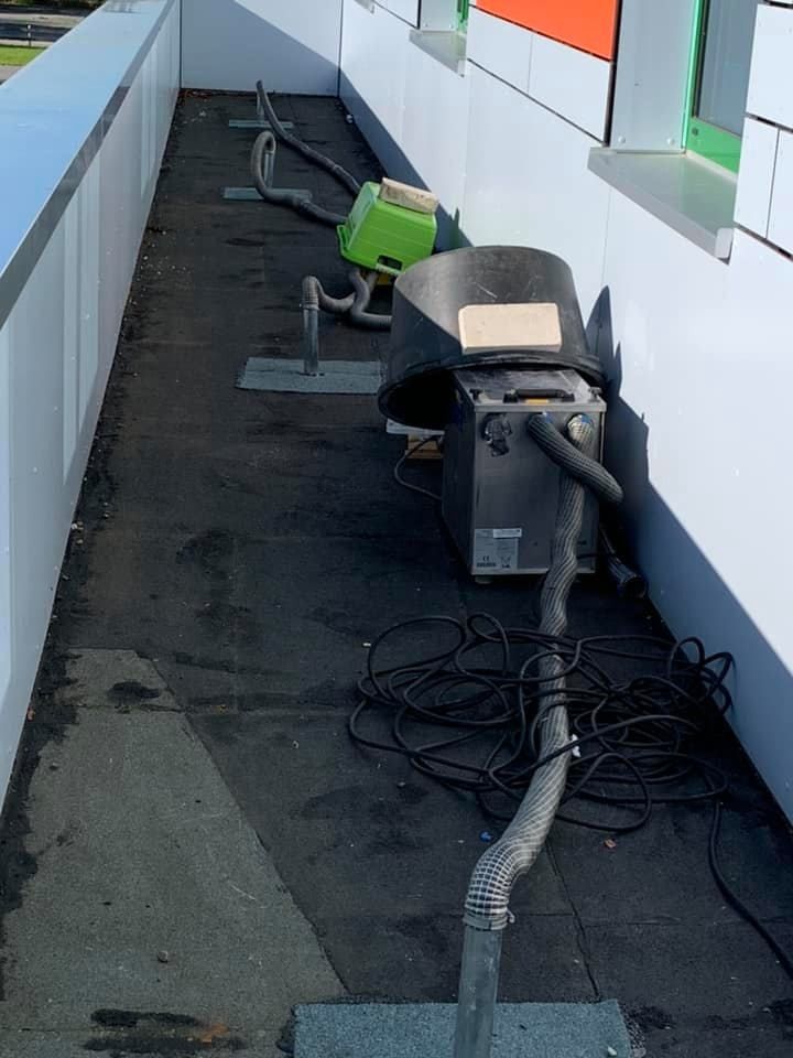 Ein mit schwarzer Dachpappe bedeckter Laufsteg, Belüftungsanlagen, Kabel und ein Werkzeugwagen eines Arbeiters.