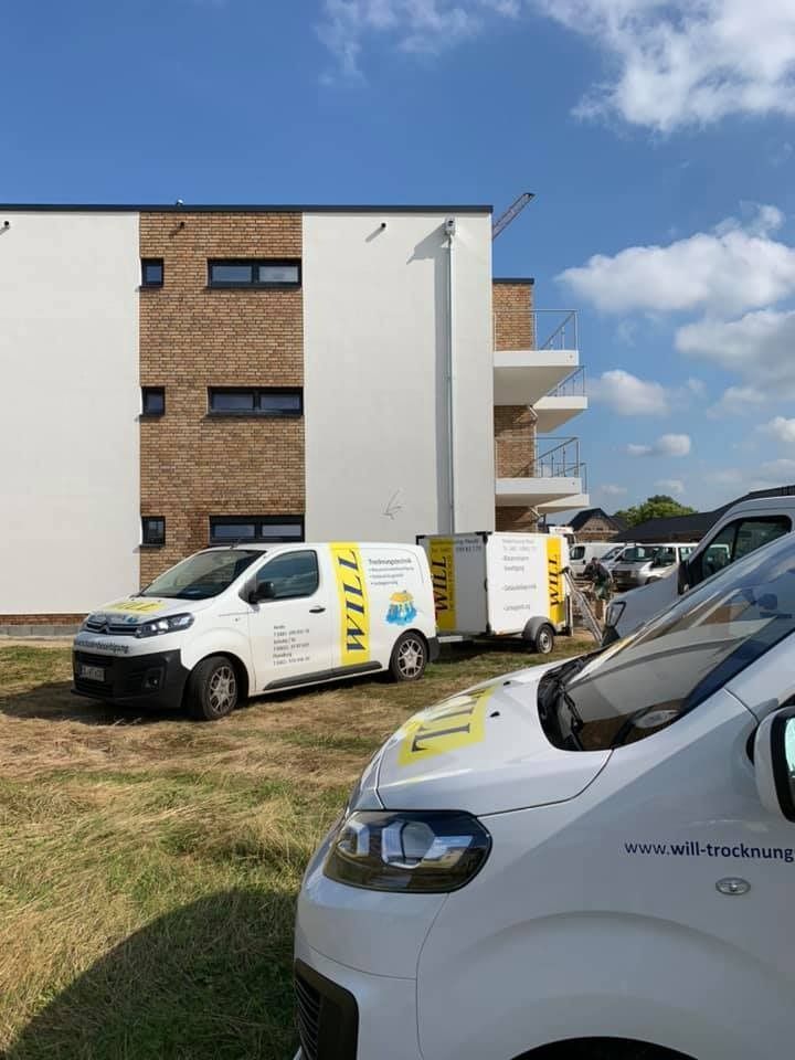 Lieferwagen parken an einem sonnigen Tag vor einem Backstein-Wohnhaus.