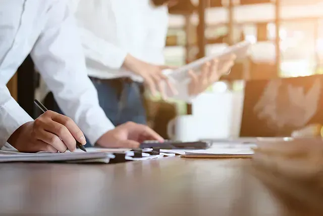 Dos personas firman papeles de divorcio en una mesa, anillos de boda colocados entre los documentos.