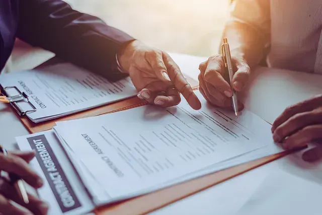 Dos personas firman papeles de divorcio en una mesa, anillos de boda colocados entre los documentos.