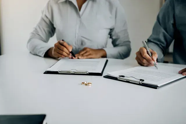 Dos personas firman papeles de divorcio en una mesa, anillos de boda colocados entre los documentos.