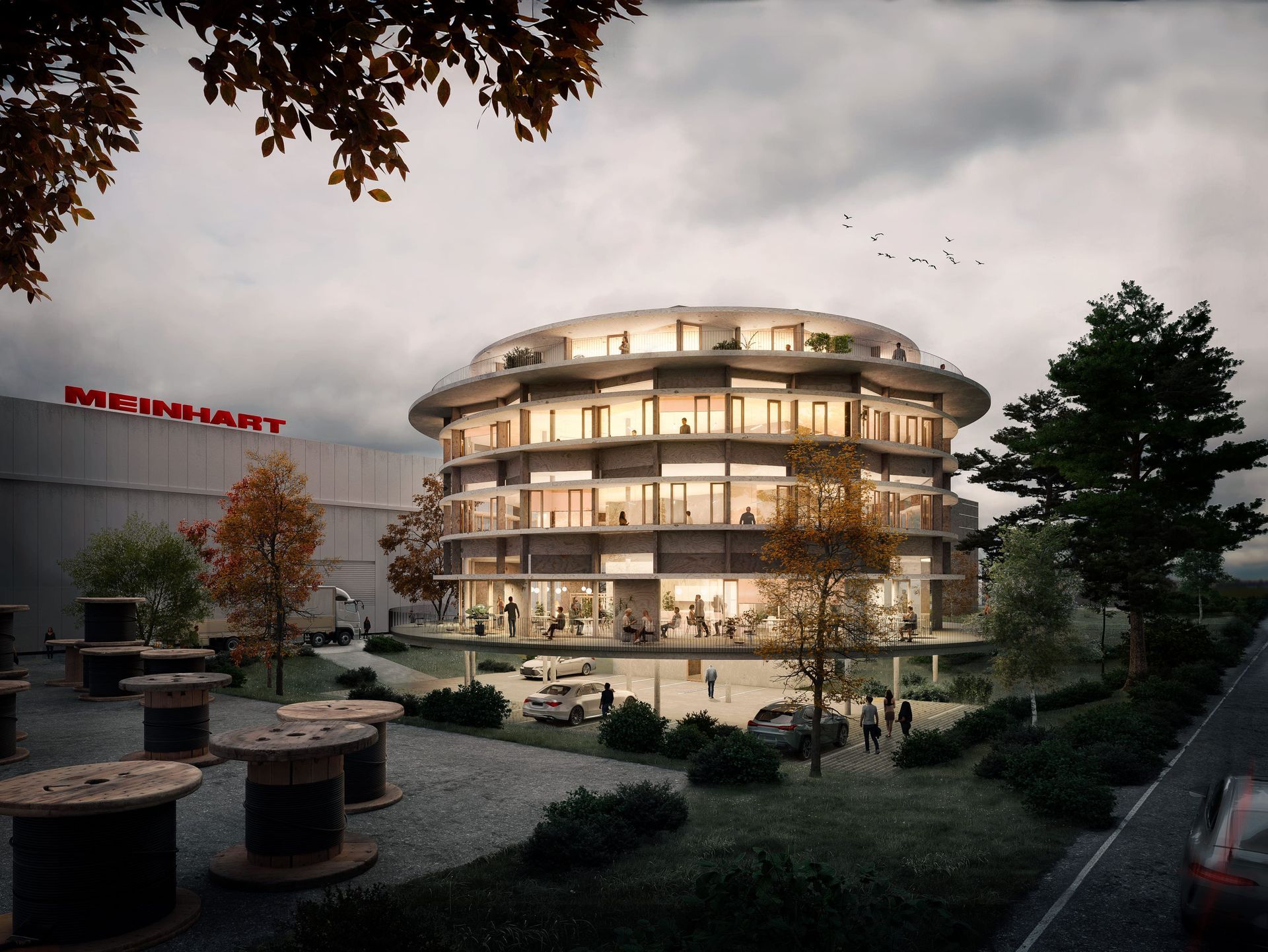 Edificio de oficinas moderno y circular de varios niveles, con árboles y coches. Se ve el letrero de 