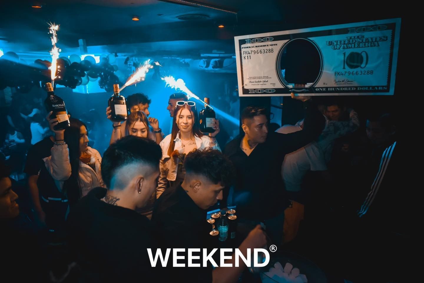 Un grupo de personas está bailando en un club con un billete de dólar en la pared.