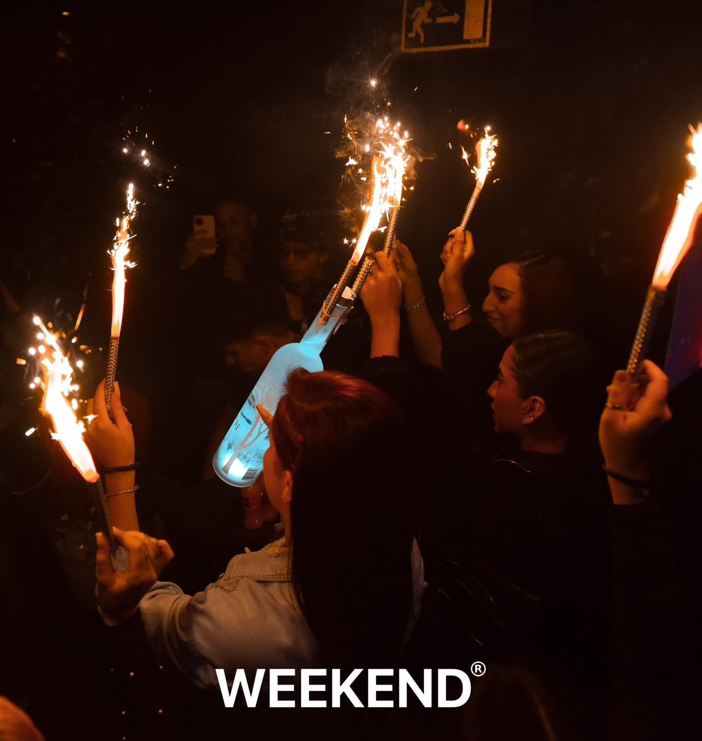 Un grupo de personas sostiene bengalas en sus manos y la palabra fin de semana está en la parte inferior.