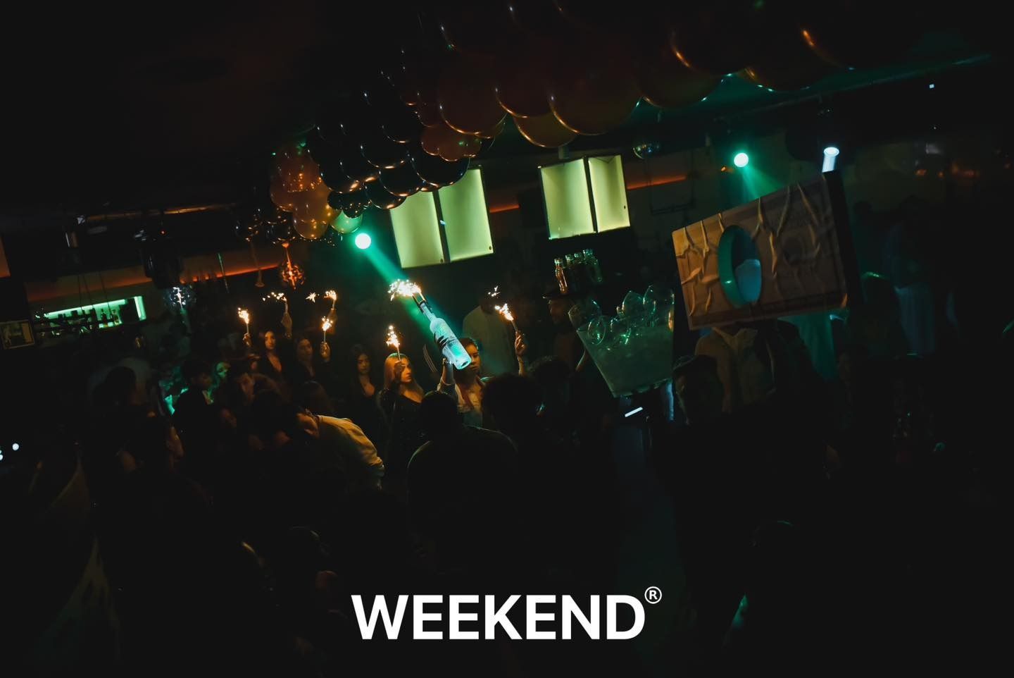 Una multitud de personas se reúne en una habitación oscura en una fiesta de fin de semana.