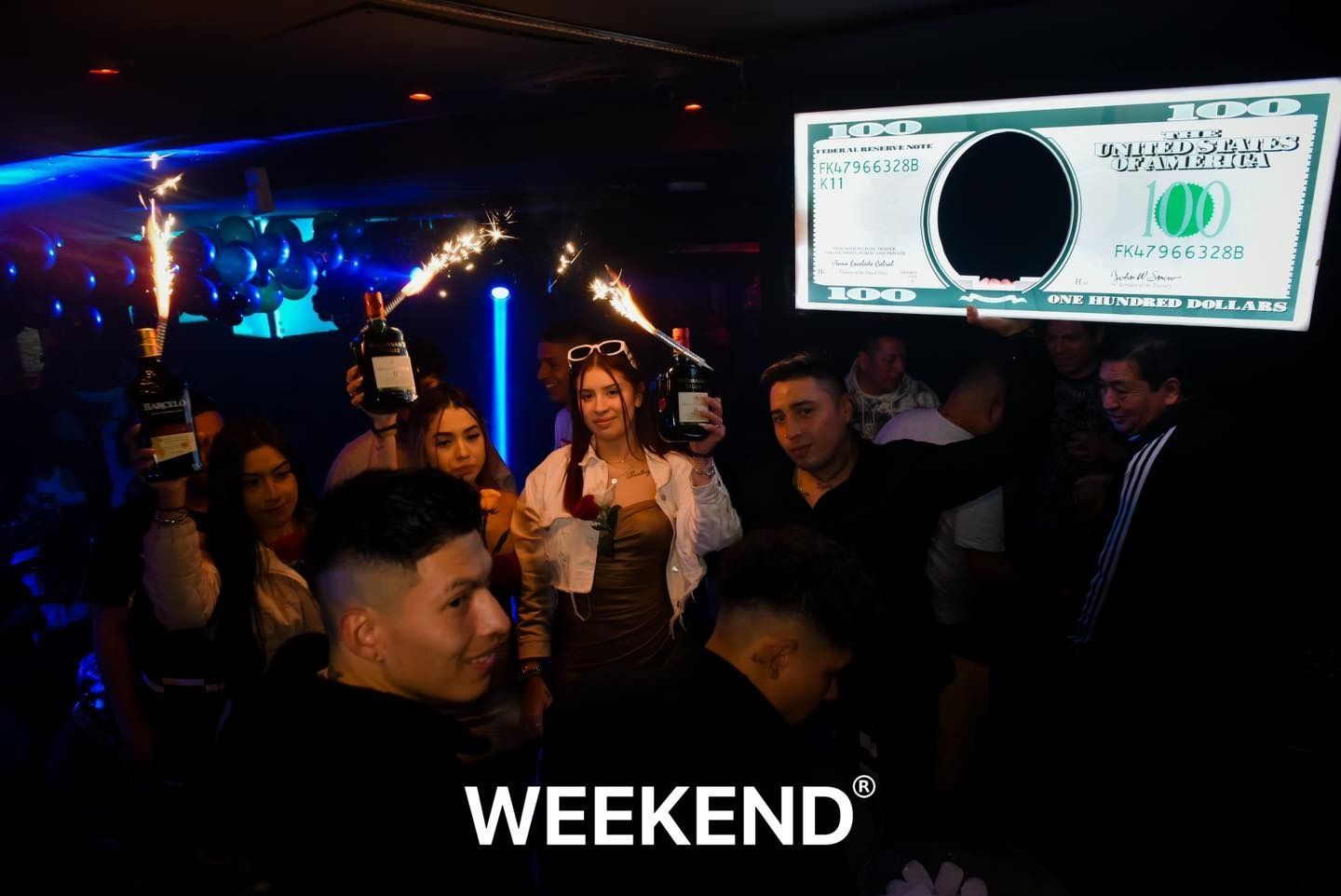 Un grupo de personas está de pie frente a un gran billete de dólar.