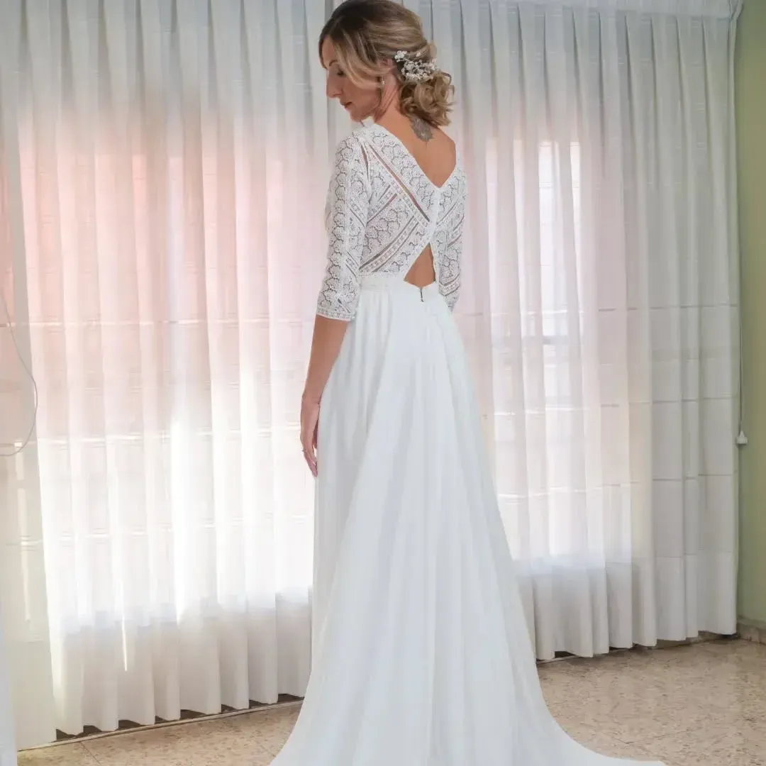 Mujer con vestido de novia blanco con mangas de encaje, de pie cerca de la ventana.