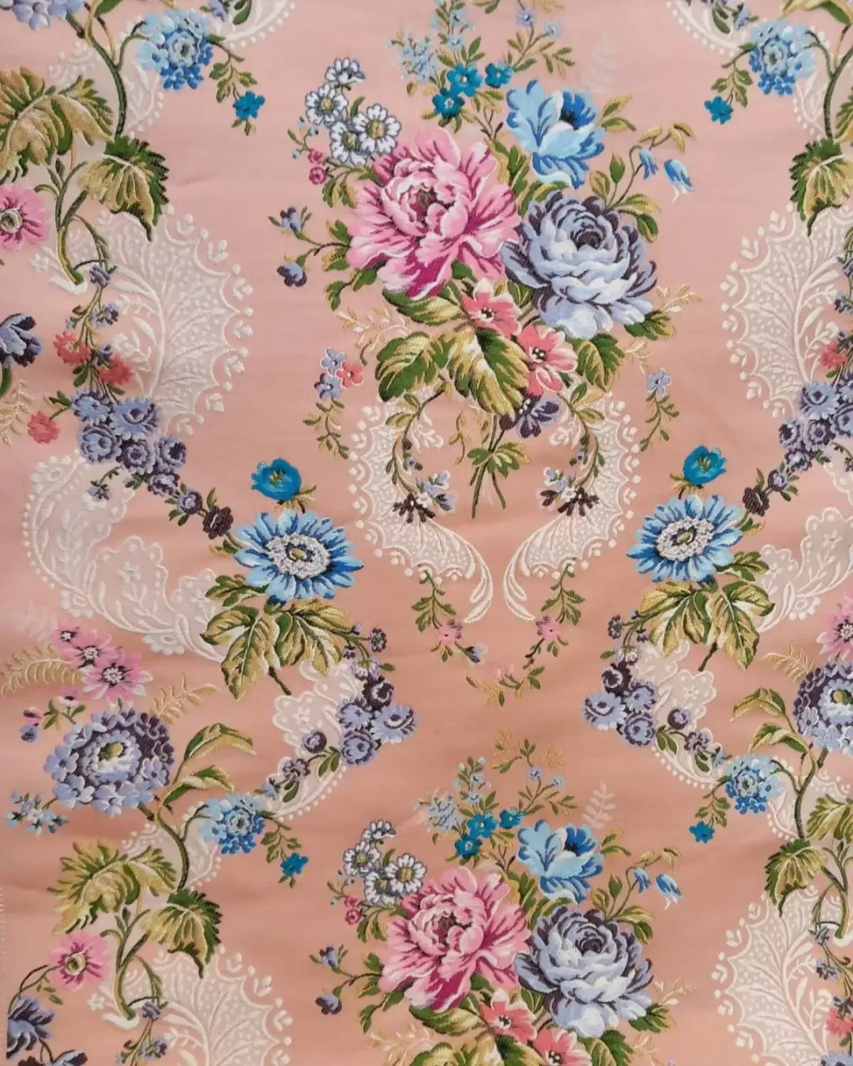 Tela floral rosa con flores azules, rosas y blancas y patrón de volutas.