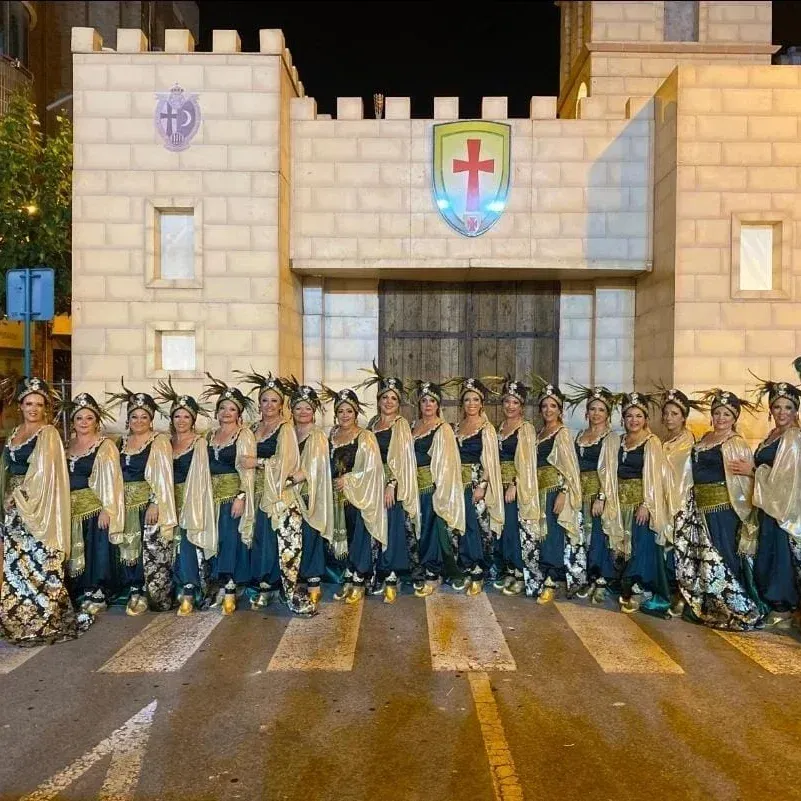 Un grupo de mujeres con trajes elaborados posan frente a la fachada de un castillo por la noche.