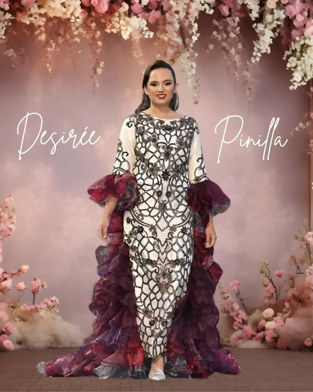 Mujer con un vestido largo de color crema con bordados negros y volantes morados en una pasarela llena de flores.