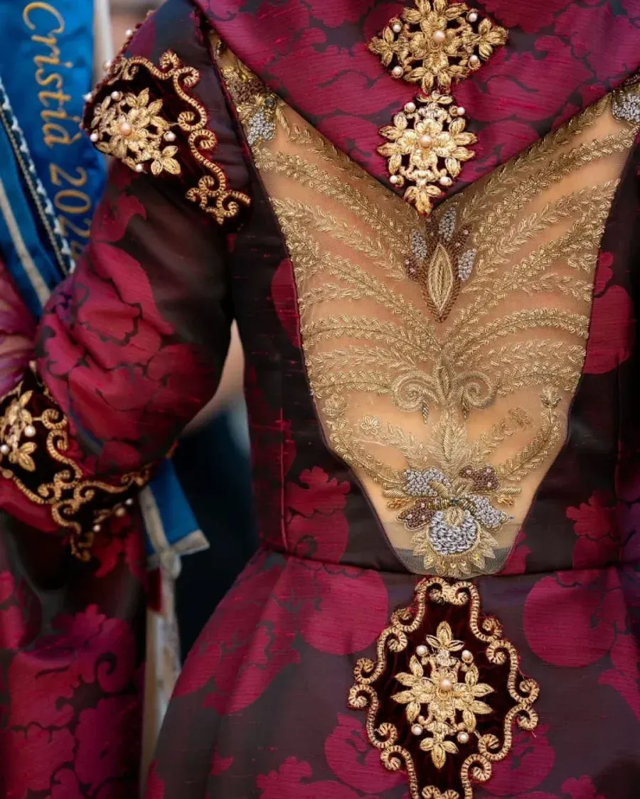 Primer plano de un traje histórico detallado en tonos burdeos y dorado con adornos ornamentados.