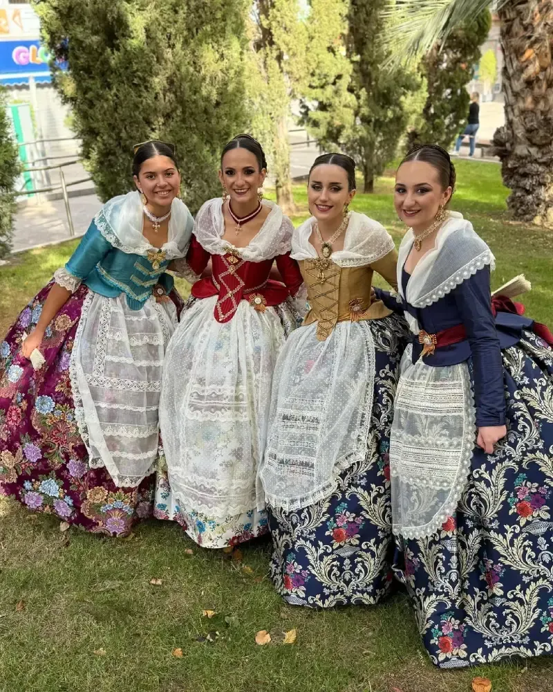 Cuatro mujeres con coloridos vestidos tradicionales valencianos posando al aire libre.