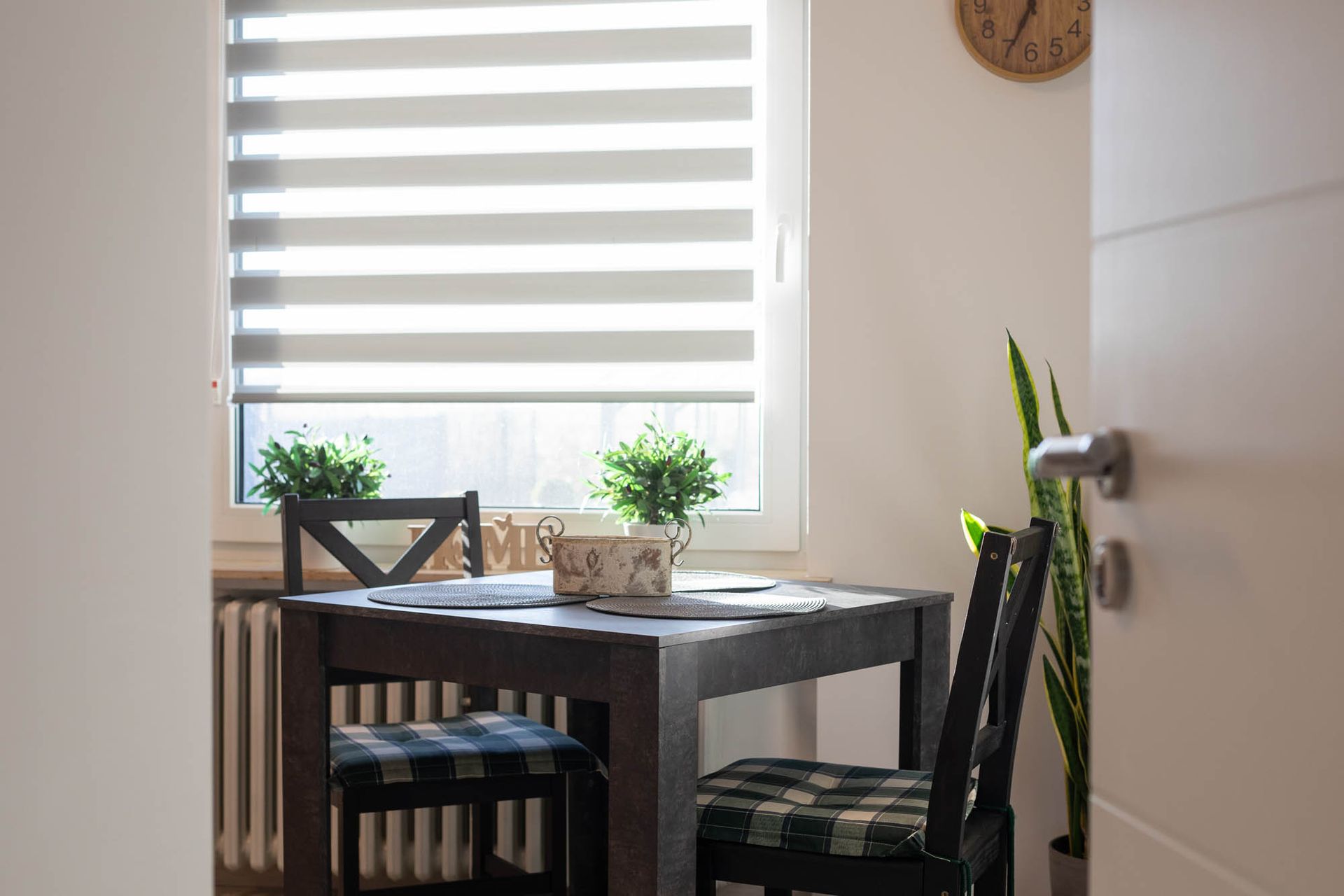 Ein Esstisch und Stühle vor einem Fenster mit einer Uhr an der Wand.