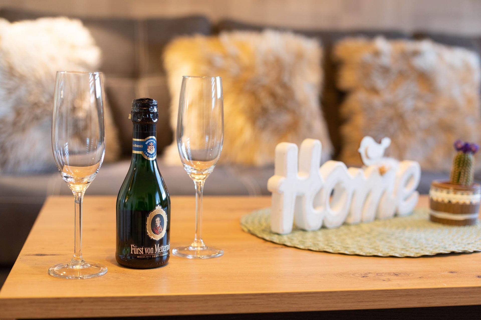 Eine Flasche Champagner und zwei Weingläser stehen auf einem Holztisch in einem Wohnzimmer.