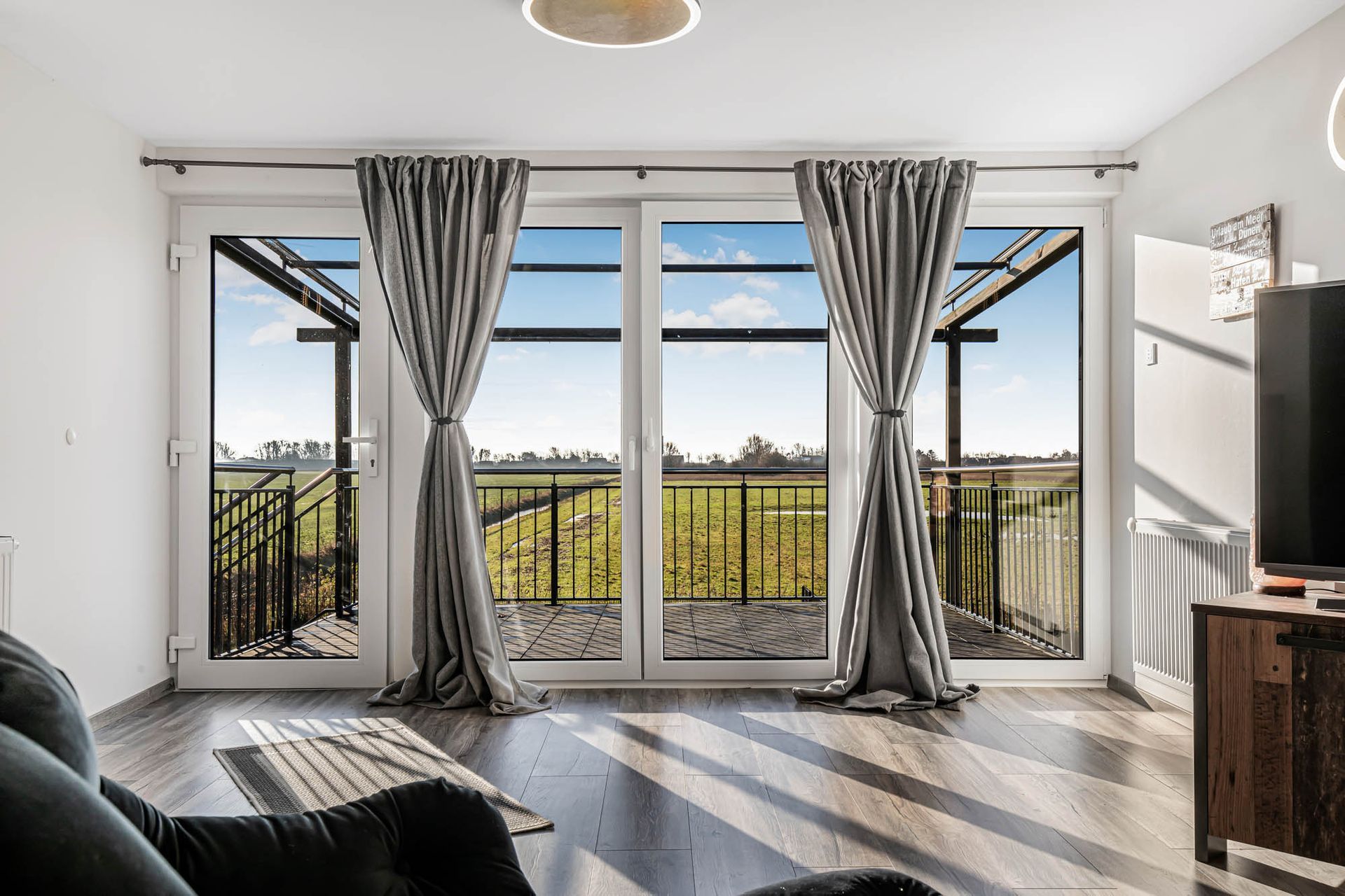 Ein Wohnzimmer mit vielen Fenstern und Vorhängen und Blick auf ein Feld.