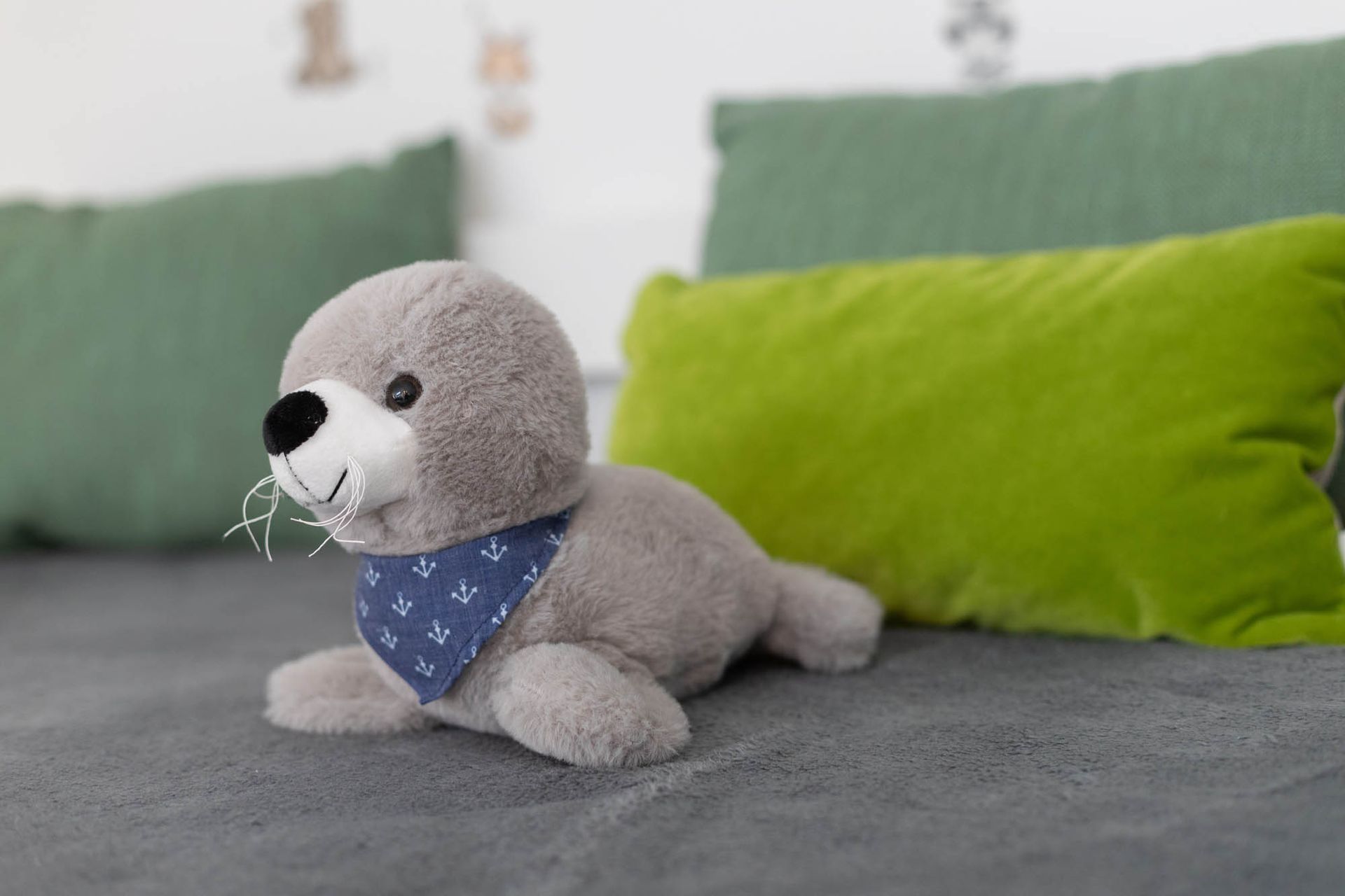 Eine ausgestopfte Robbe sitzt auf einem Bett neben einem grünen Kissen.