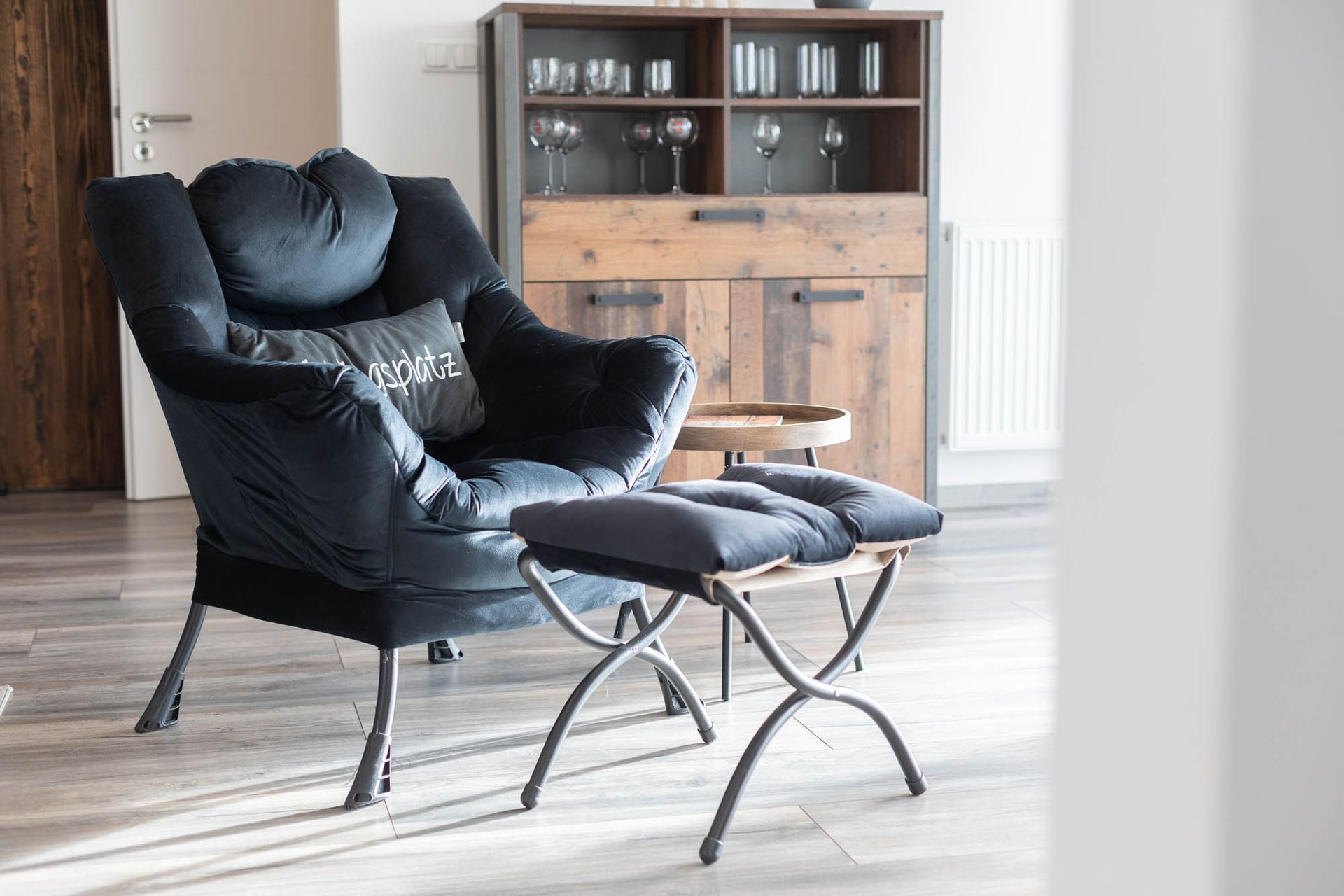 Im Wohnzimmer gibt es einen Sessel und einen Ottomanen.