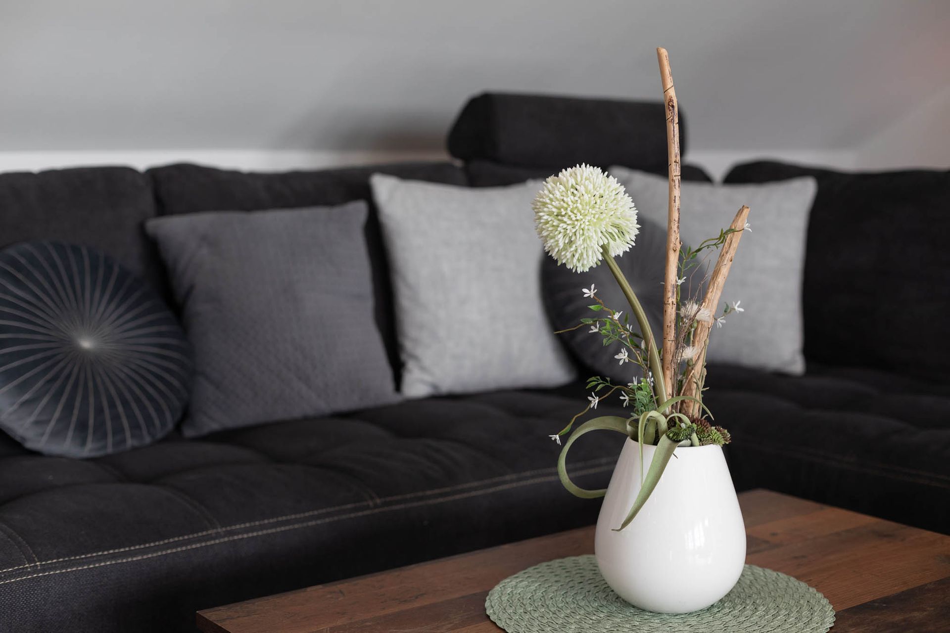 Eine Vase mit Blumen steht auf einem Tisch vor einem Sofa.