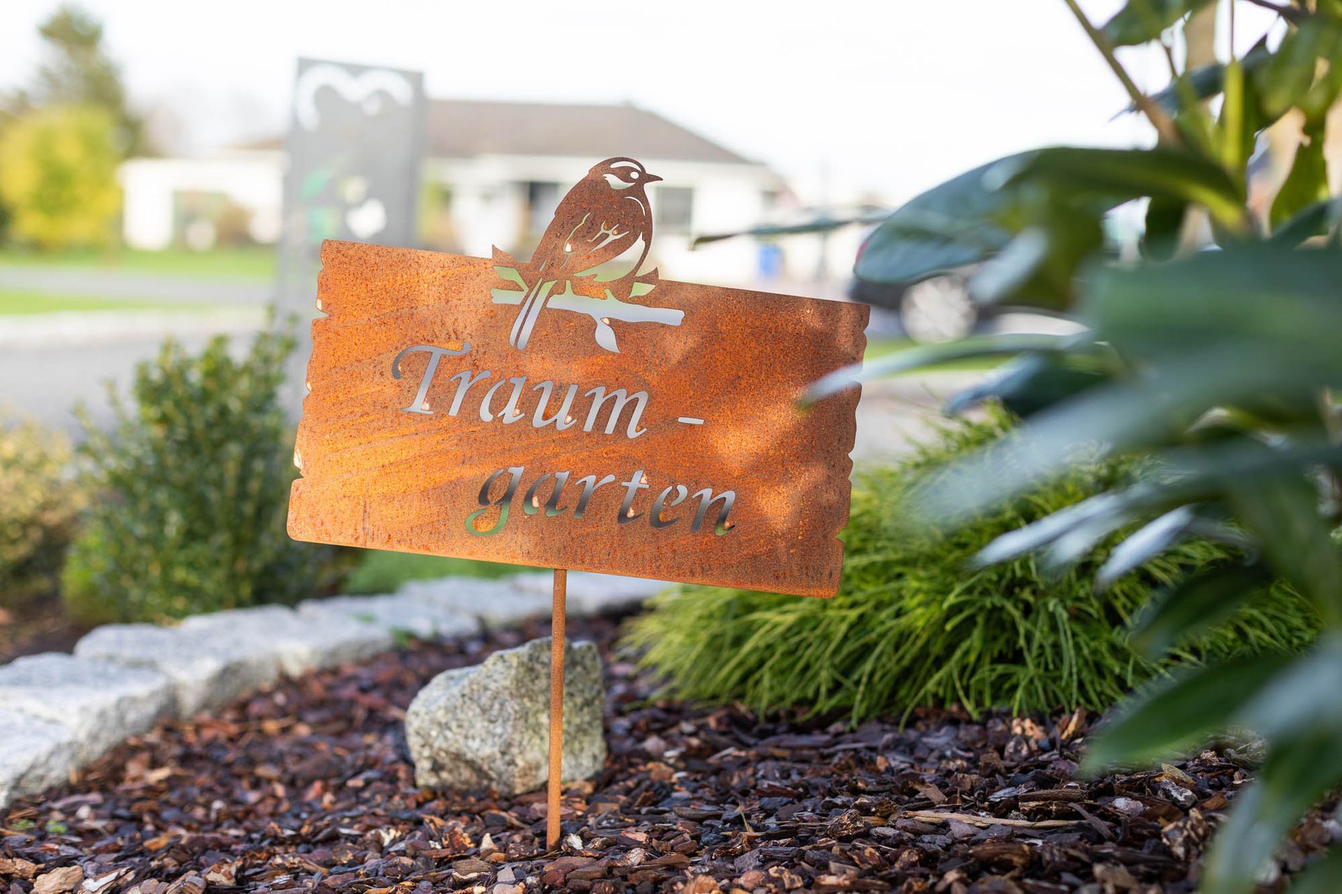 In einem Garten steht ein rostiges Schild mit einem Vogel darauf.