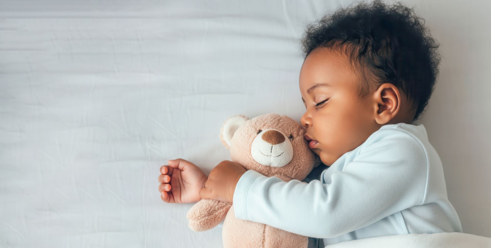 Bébé endormi serrant un ours en peluche dans ses bras sur un lit blanc