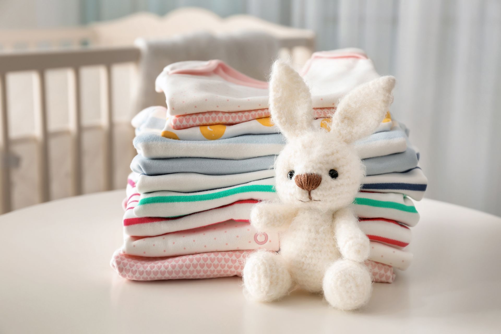Lapin en peluche blanc devant des vêtements de bébé pastel pliés sur une table
