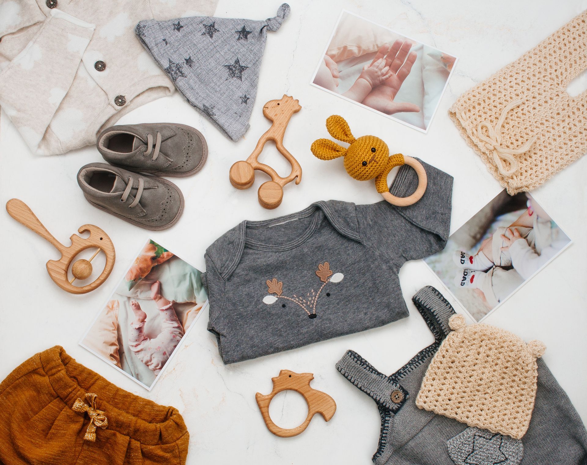 Vêtements et accessoires pour bébé disposés sur fond blanc, comprenant des tricots, des chaussons, des jouets et des photos.