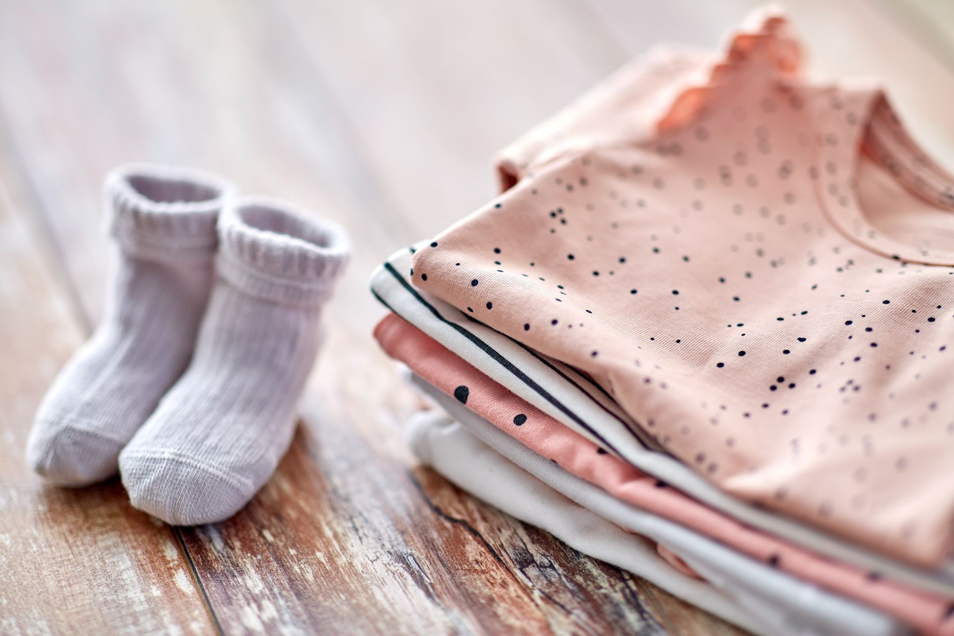Vêtements de bébé roses pliés et chaussettes blanches sur une surface en bois rustique