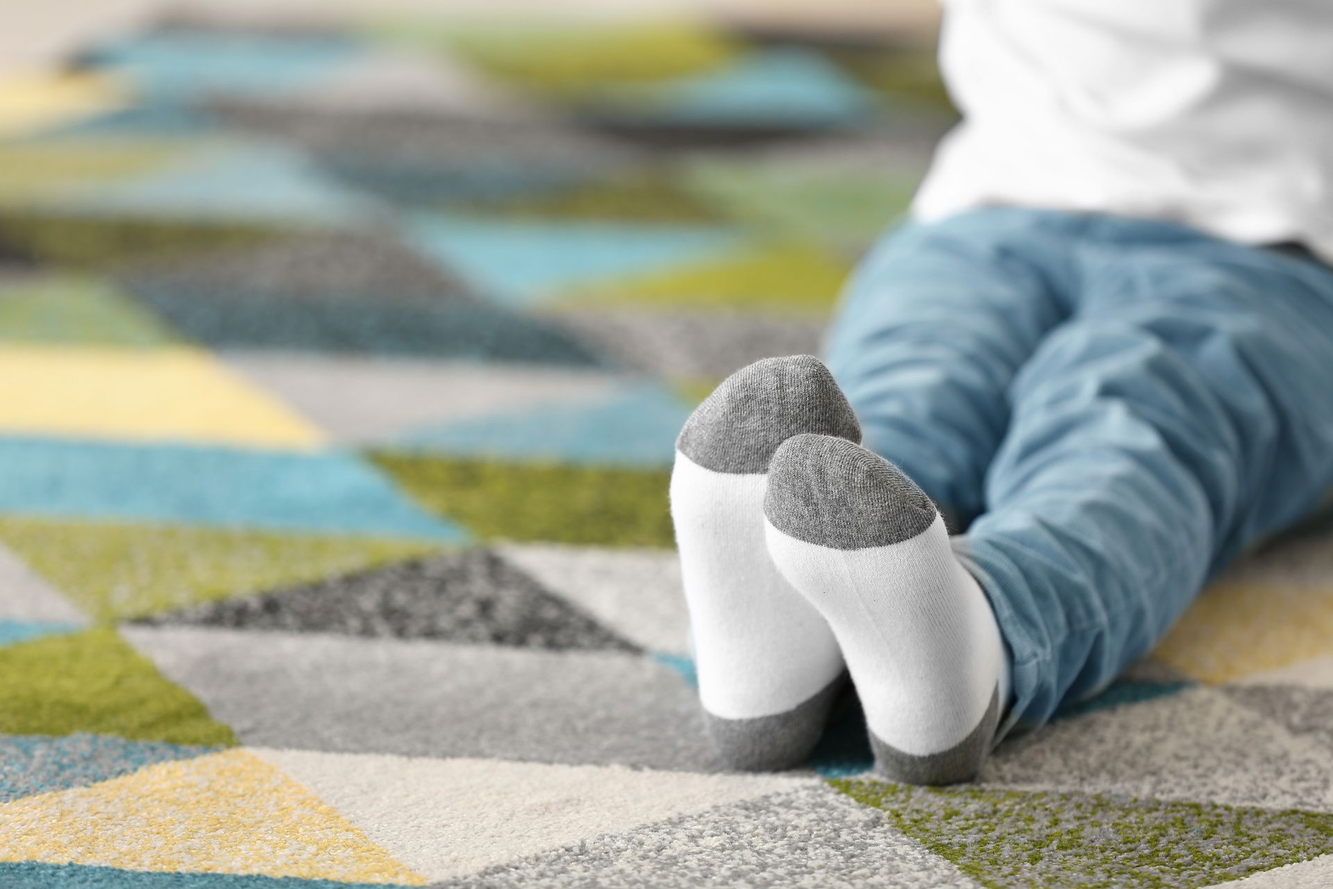 Personne allongée sur un tapis géométrique coloré, portant un jean bleu et des chaussettes blanches à bout gris.