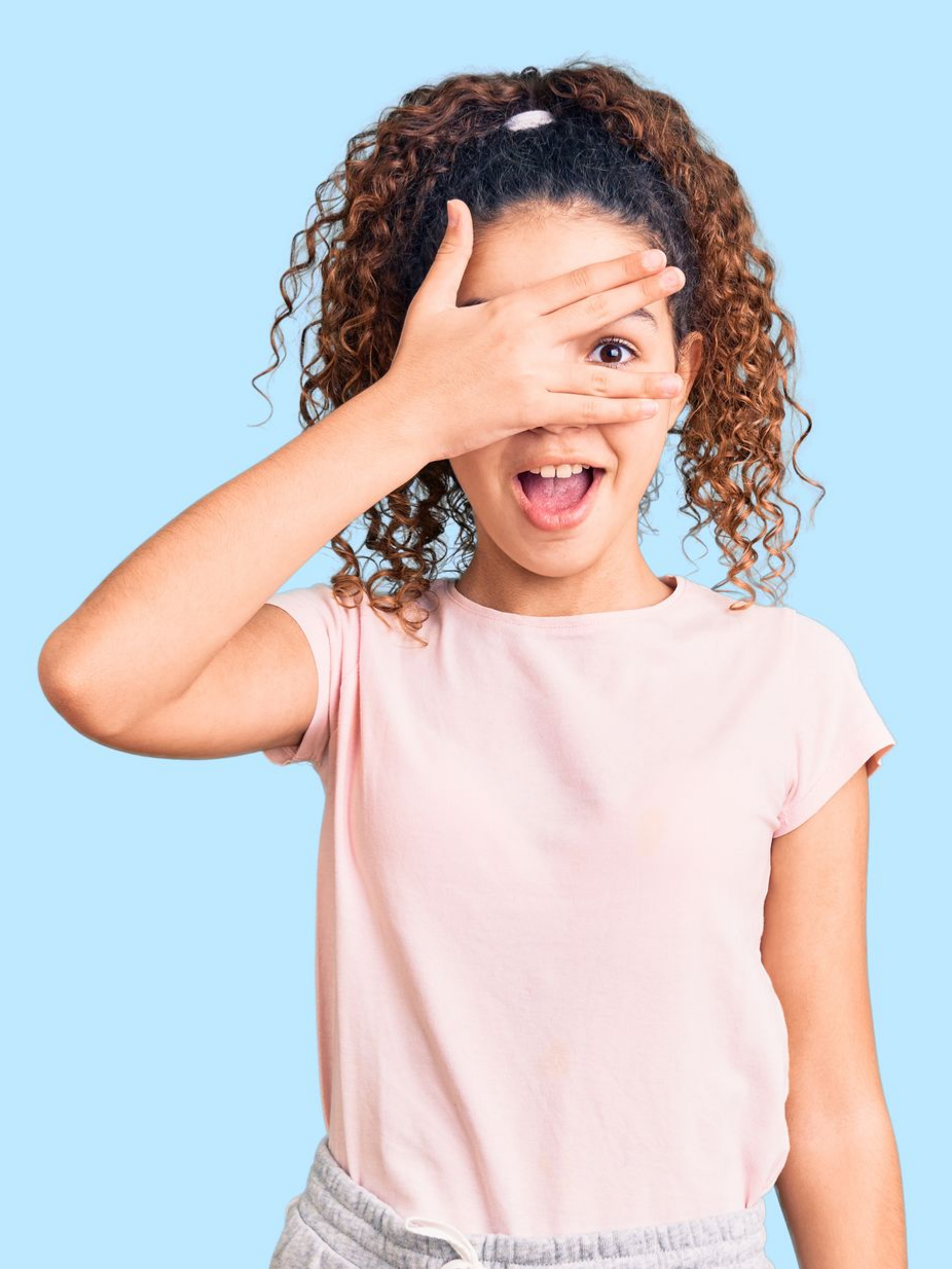 Fille en chemise rose se cachant un œil avec sa main sur un fond bleu clair