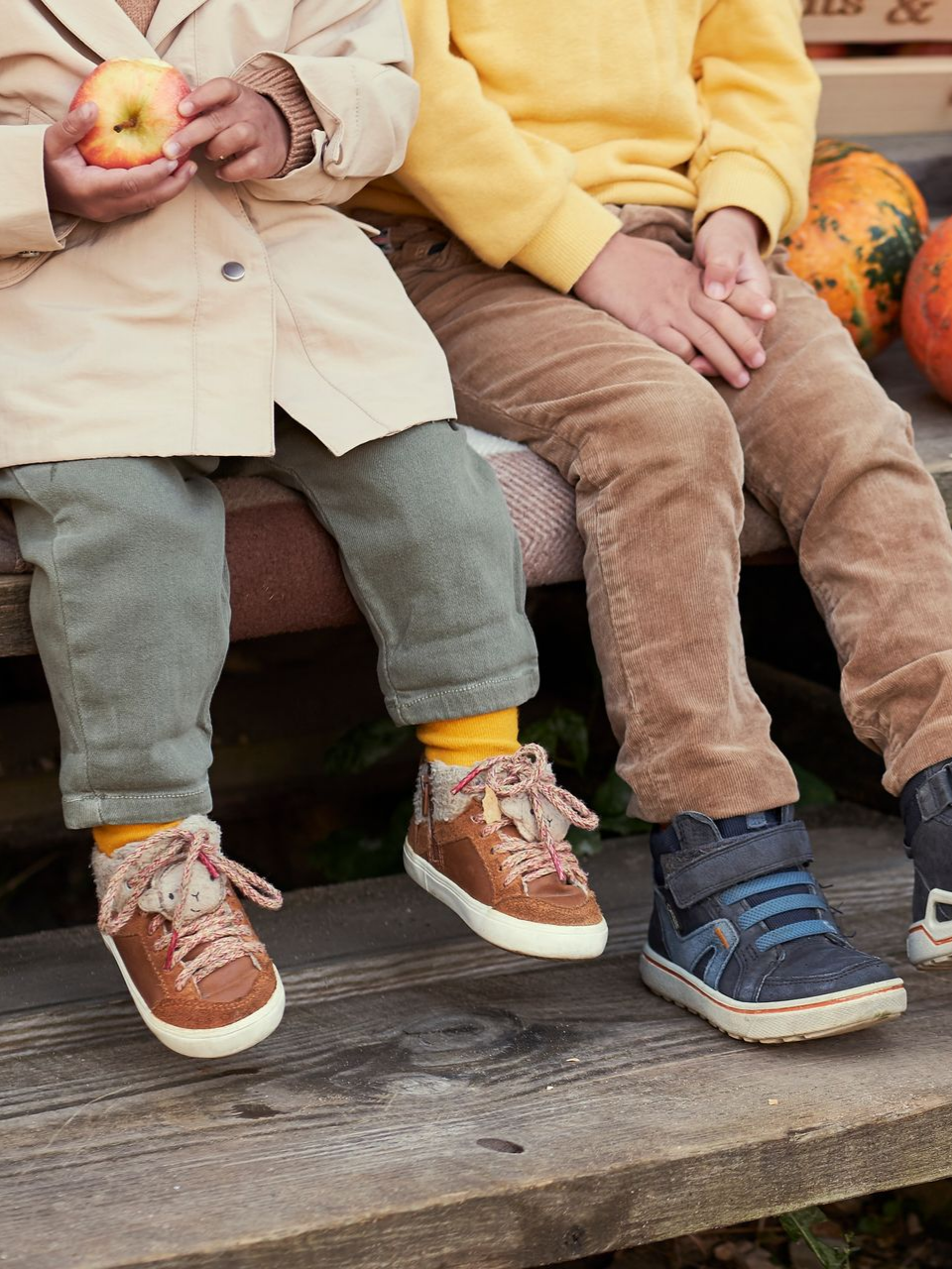 Deux enfants sont assis sur un banc, tenant des pommes, vêtus de vêtements d'automne confortables et de bottes.